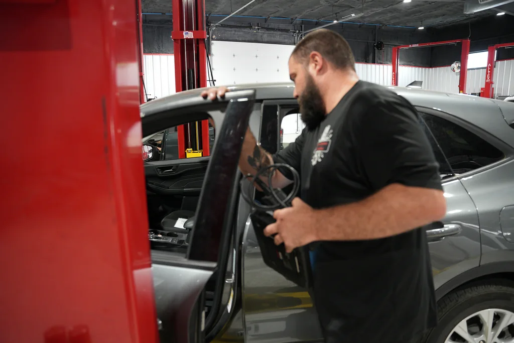 Technician holding diagnostic equipment beside an open vehicle door.
