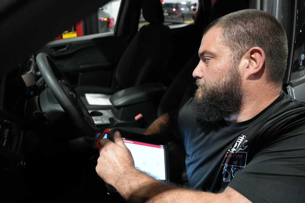 Technician using a diagnostic tablet inside a vehicle.