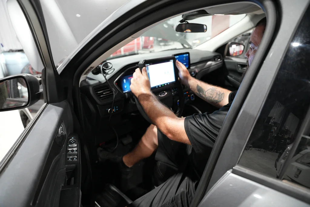 View through the open driver door of a technician using a diagnostic tablet.