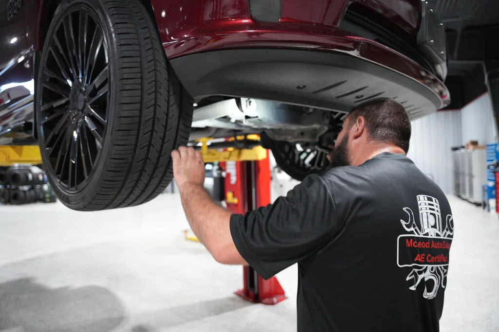 Technician inspecting the underside of a raised vehicle near the front wheel.