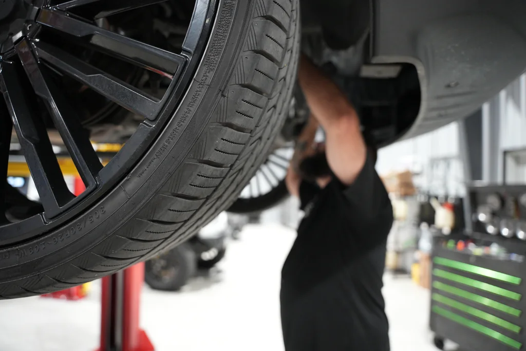 Close view of a front wheel with a technician working beneath the raised vehicle.