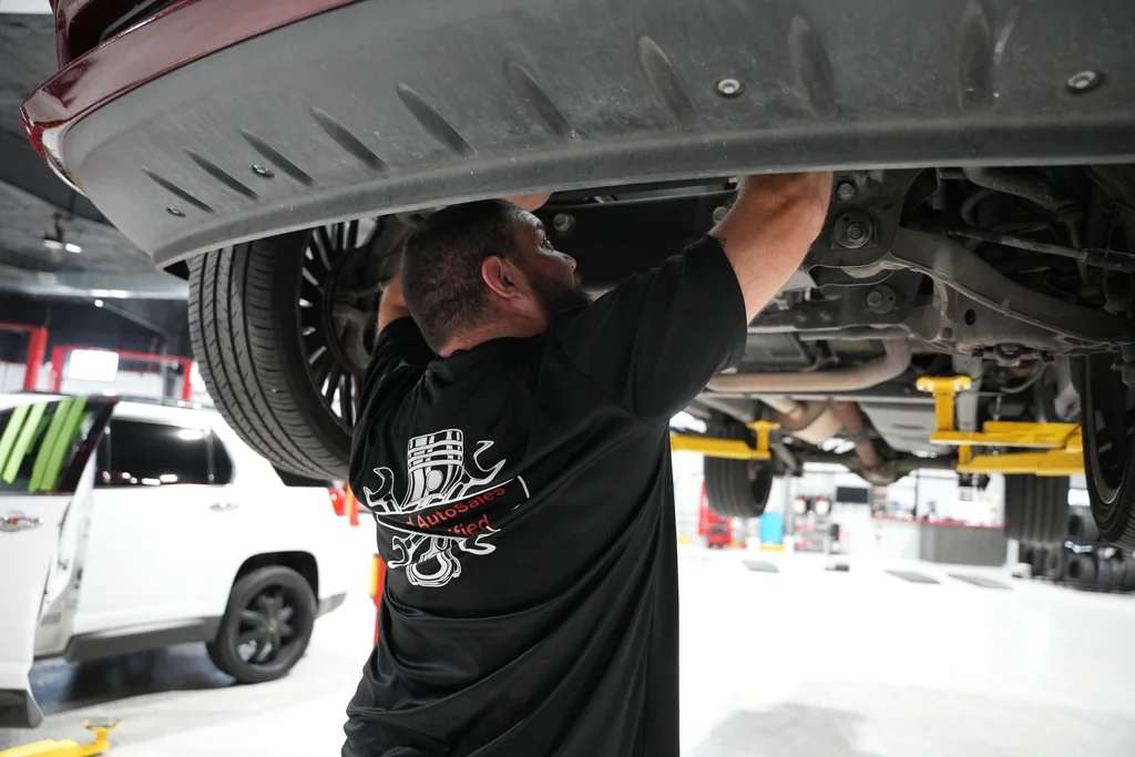 Technician reaching toward the underside of a vehicle on a lift.